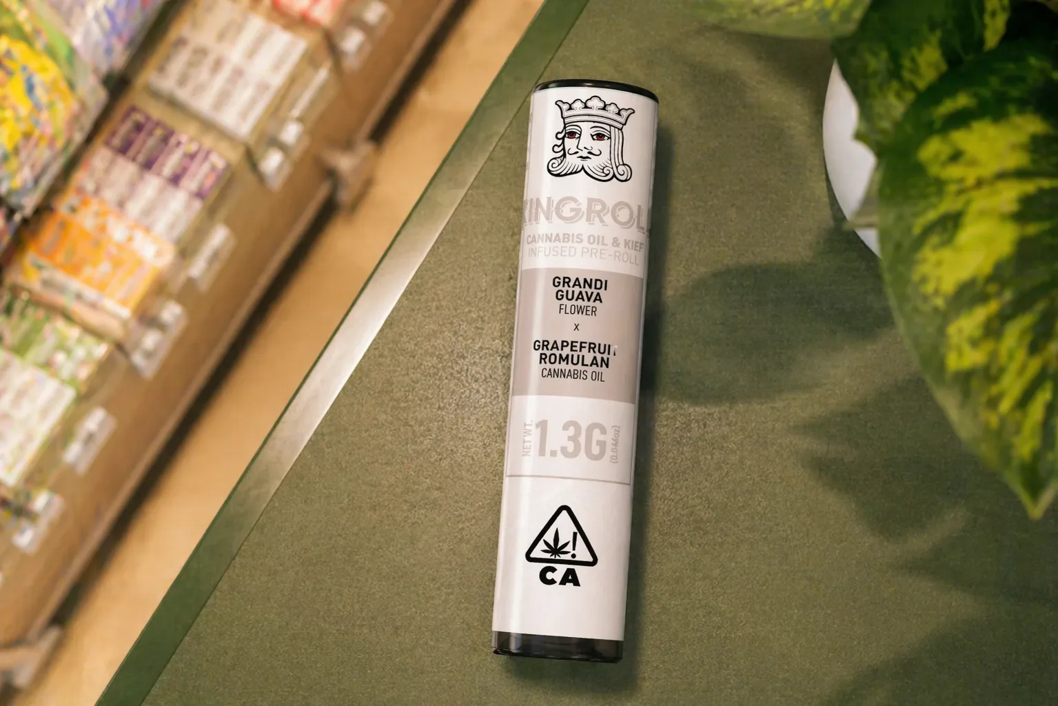 Top view of Kingroll infused pre roll tube with grandi guava and grapefruit romulan strains on a dispensary counter near a plant