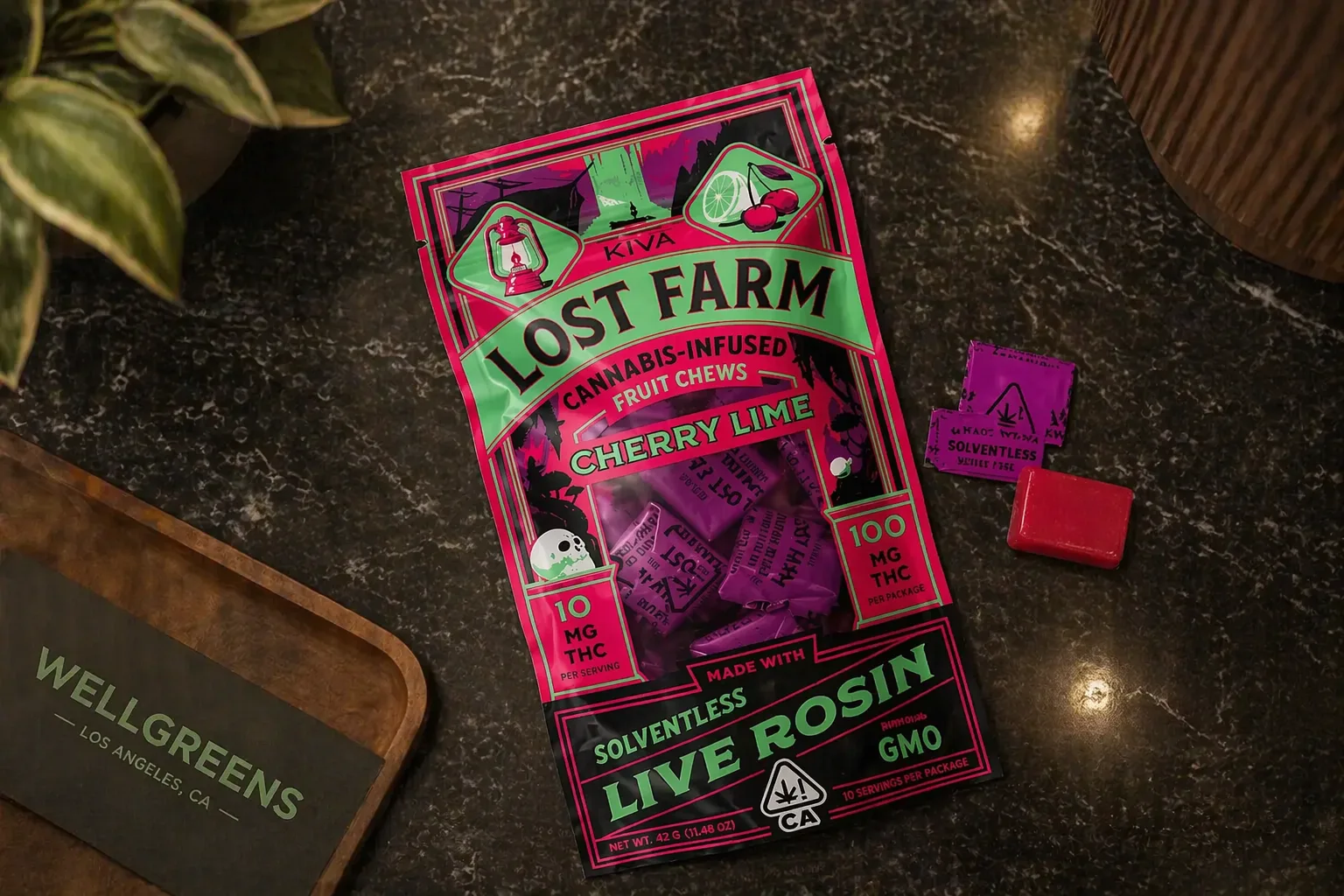 Top view of Lost Farm cherry lime live rosin infused fruit chews packaging with individual pieces on a counter near a Wellgreens display