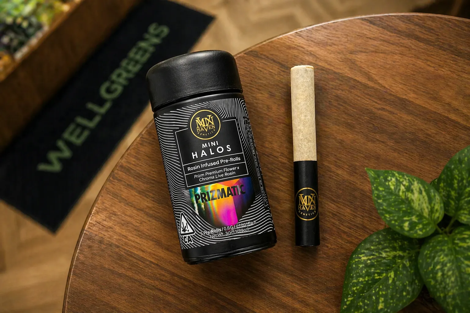 Top view of Maven Mini Halos prizmatic infused pre rolls container and preroll on a wooden table near a plant and Wellgreens mat